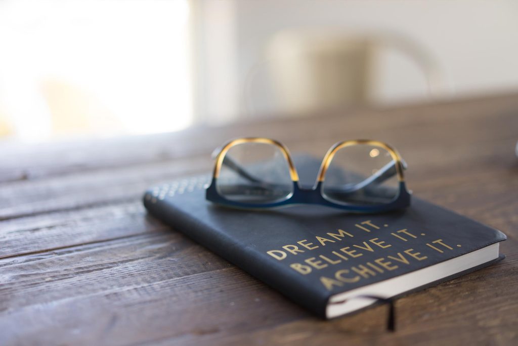 wooden table with a book on it then glasses balancing on the book
