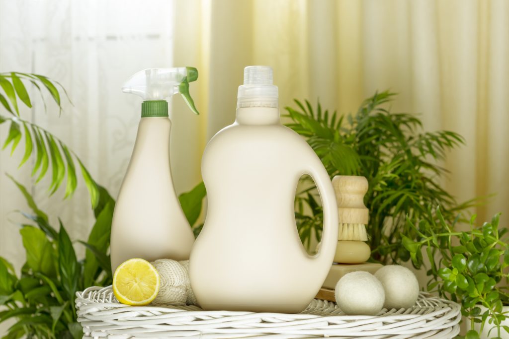 Natural cleaners, cleaning products, natural detergent bottles with soap, lemon and brush on wooden podium in home interior with home plants. Mockup for natural detergents and cleaning products